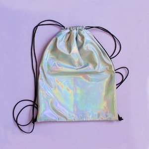 Puede incluir: Una bolsa de cordón de color plateado iridiscente con cordones negros. La bolsa está hecha de un material brillante y reflectante.