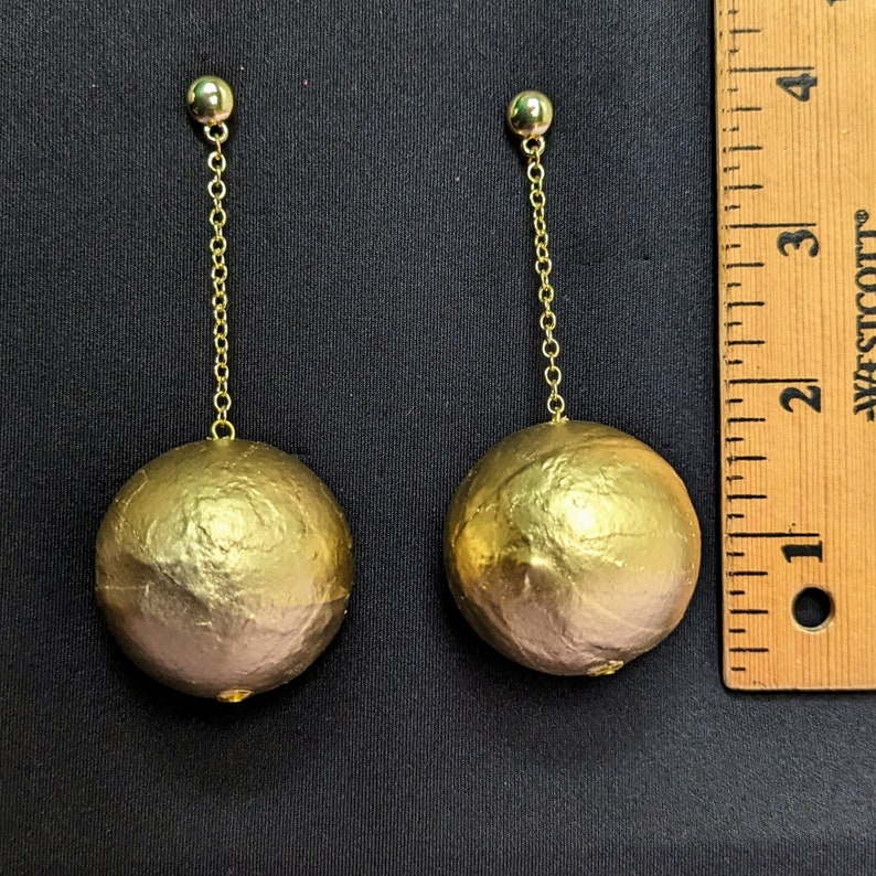 a pair of ball dangle earrings next to a ruler