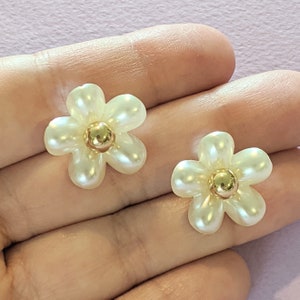 a pair of white flower shaped earrings on a hand