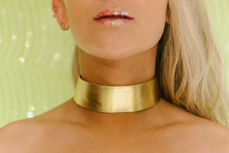 a woman wearing a gold choker with a green background
