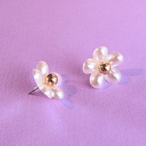 a pair of white flower shaped earrings on a purple background