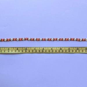 The fully extended beaded choker necklace is laid out next to a yellow measuring tape.