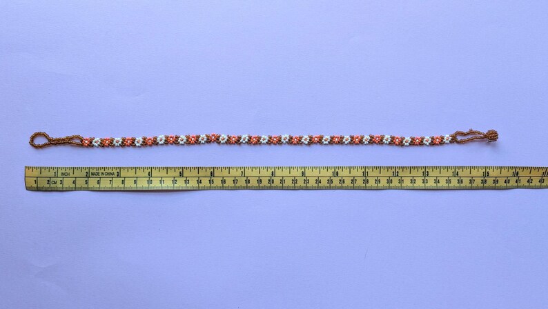 The fully extended beaded choker necklace is laid out next to a yellow measuring tape.