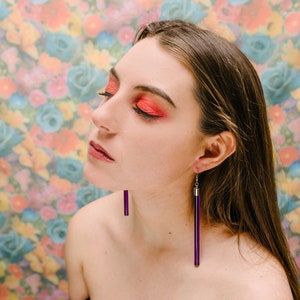 a woman with red eye makeup and purple earrings