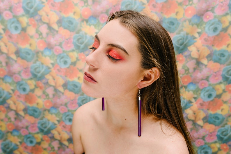 a woman with red eye makeup and purple earrings