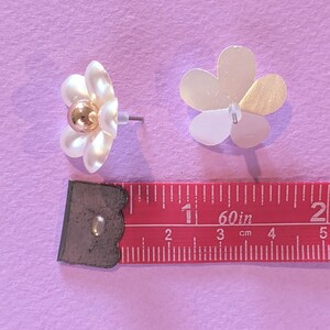 a pair of white floral earrings next to a ruler