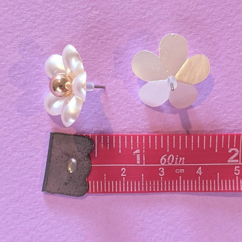 a pair of white floral earrings next to a ruler