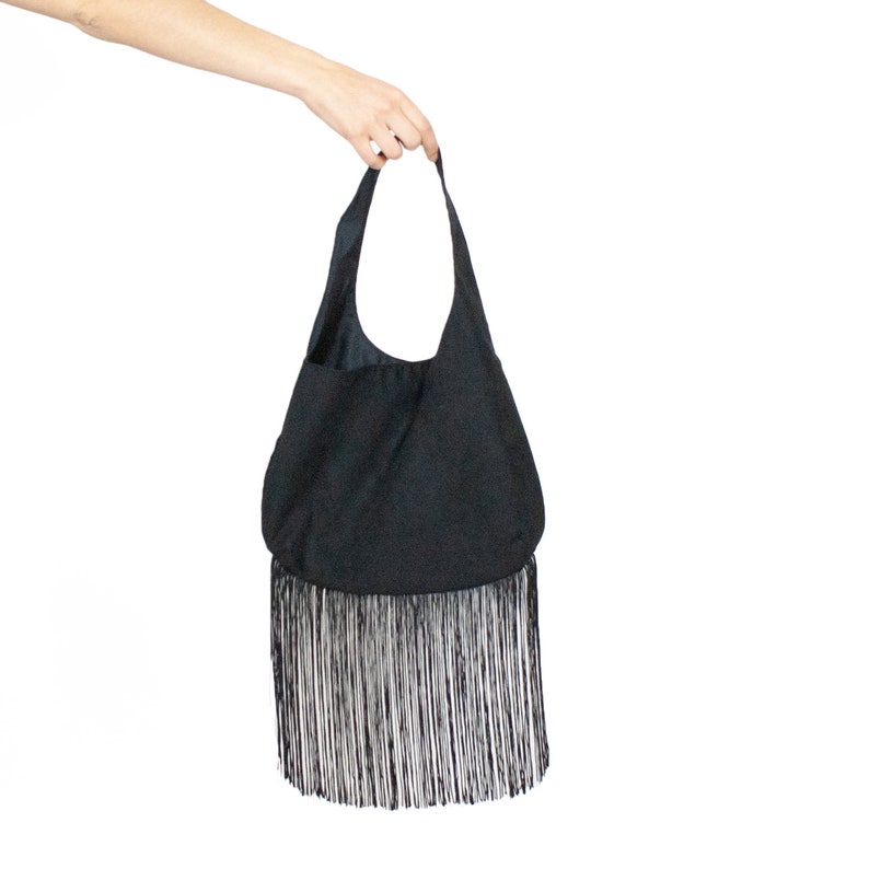 a hand holding a black bag with a fringe
