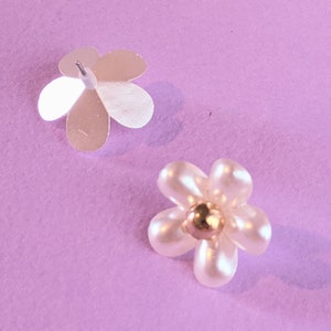 a pair of white flower shaped earrings on a purple background