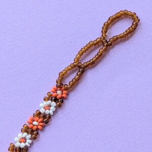 A close-up view displays the looped end of the brown seed bead strand and adjacent flower beads.