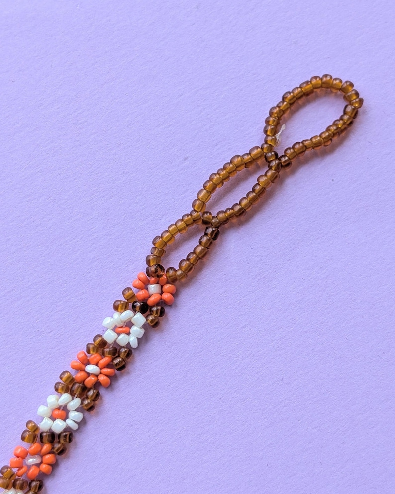 A close-up view displays the looped end of the brown seed bead strand and adjacent flower beads.