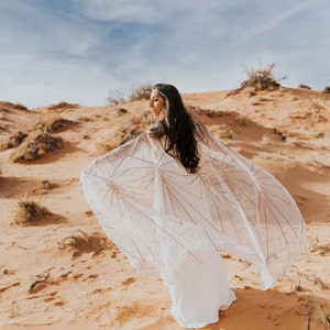 a woman in a white dress is standing in the sand