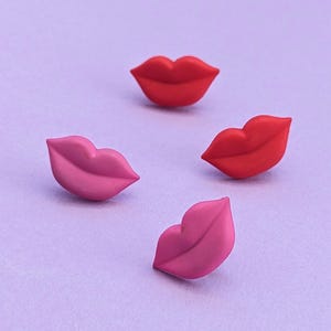 May include: Four colorful lips-shaped buttons in red and pink. The buttons are made of a smooth, glossy material and have a slightly raised lip shape.