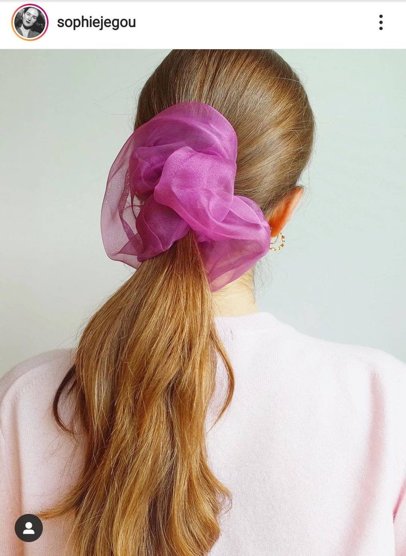 a woman with long hair in a ponytail wearing a pink sweater