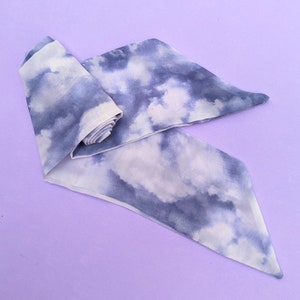 May include: A white and blue tie-dye fabric scarf with a cloud pattern. The scarf is folded and tied in a knot.
