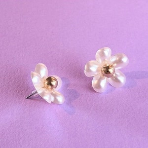 a pair of white flower shaped earrings on a purple background