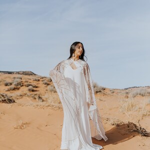 a woman standing in the desert wearing a long cape