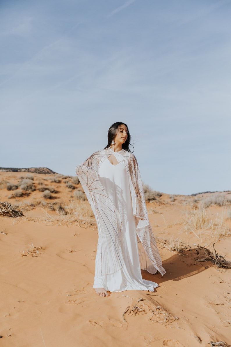 a woman standing in the desert wearing a long cape