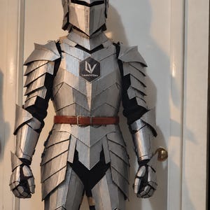 Op de afbeelding: Een volledig zilverkleurig harnas met een helm, schouderstukken, handschoenen en beenplaten over een zwarte basislaag. Een bruine leren riem wordt in de taille gedragen. Een zwarte zeshoekige patch met de tekst LV LaunchVibes is zichtbaar op het borstpantser.