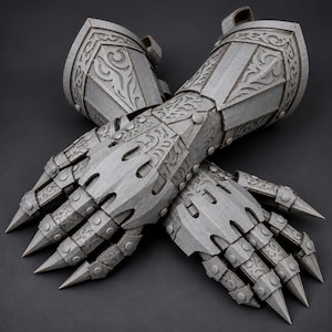 May include: A pair of articulated gauntlets crafted from grey corrugated cardboard, featuring intricate laser-cut filigree patterns, layered plate construction, and pointed finger tips, designed to cover the hands and forearms.