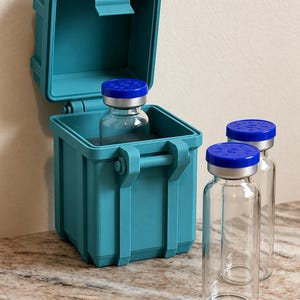 May include: A teal, square, hinged storage container with a latch, holding one clear glass vial with a blue cap. Two additional identical glass vials with blue caps stand upright next to the container on the surface.