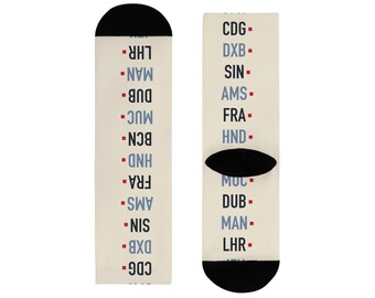 Könnte beinhalten: Ein Paar cremefarbene Socken mit einer vertikalen Liste von Flughafencodes in abwechselnd schwarzem und blauem Text. Jeder Code ist durch ein kleines rotes Quadrat getrennt. Die Socken haben schwarze Zehen- und Fersenbereiche mit Codes wie CDG, DXB, SIN, AMS, FRA, HND, BCN, MUC, DUB, MAN und LHR.