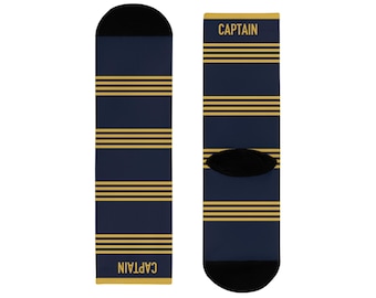Könnte beinhalten: Ein Paar marineblaue Socken mit vier Sätzen aus drei horizontalen goldenen Streifen. Das Wort CAPTAIN ist in goldenen Großbuchstaben oben und unten auf den Socken aufgedruckt. Die Zehen- und Fersenbereiche sind in einem soliden Schwarz gehalten.