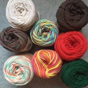 May include: Eight skeins of yarn arranged in a circular pattern. The collection includes solid colors in cream, dark brown, bright red, and forest green, alongside variegated skeins featuring blends of teal, yellow, pink, orange, and brown.