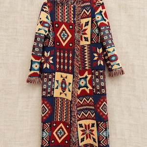 May include: A long-sleeved open-front coat featuring a multi-colored patchwork pattern with geometric shapes, diamonds, and star motifs in shades of red, navy blue, and cream. The garment is finished with frayed fringe trim along the collar and edges.