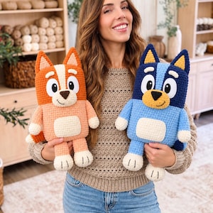 May include: Two handmade crochet plush toys featuring cartoon dog characters. One toy is orange and cream with pointed ears, while the other is blue and dark blue with pointed ears. Both have large white eyes, black noses, and cream-colored bellies.