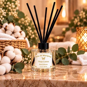 May include: A clear glass reed diffuser bottle with a black cap and six black reeds. The label reads Alas de Mariposa, Clean Cotton, Reed Diffuser, 3.5 oz / 100 mL, featuring a small butterfly icon and gold decorative borders.