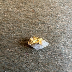 May include: A small, raw mineral specimen featuring a jagged, metallic gold-colored deposit embedded within a translucent, off-white quartz crystal. The piece has an irregular, organic shape with sharp, crystalline edges and a textured surface.