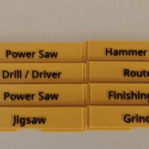 May include: Eight rectangular yellow plastic labels with black text. The labels are arranged in two columns and four rows, featuring the words Power Saw, Hammer Drill, Drill / Driver, Router, Power Saw, Finishing Gun, Jigsaw, and Grinder.