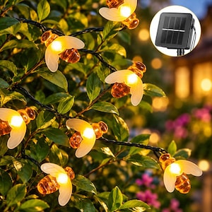 May include: A string of bee-shaped LED lights featuring translucent white wings and amber-colored bodies that glow with a warm yellow light. The lights are connected by a black wire and include a small black solar panel for power.