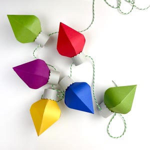 May include: A string of paper lightbulb ornaments in green, red, purple, blue, and yellow. The lightbulbs are connected with twine.