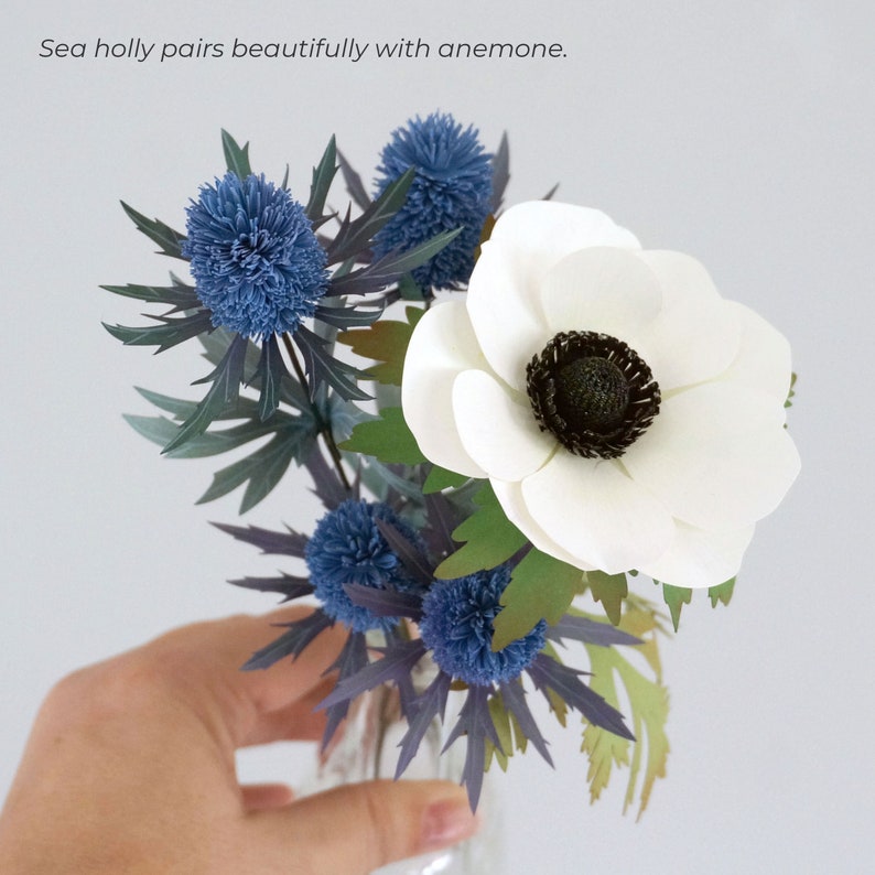 May include: A bouquet of white anemones and blue sea holly flowers in a clear glass vase.