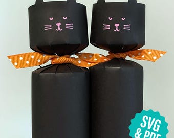 May include: Two black paper cat-shaped party crackers with pink facial features and orange polka dot ribbon. The crackers are cylindrical with a cat face design on top. The image includes the text "SVG & PDF".