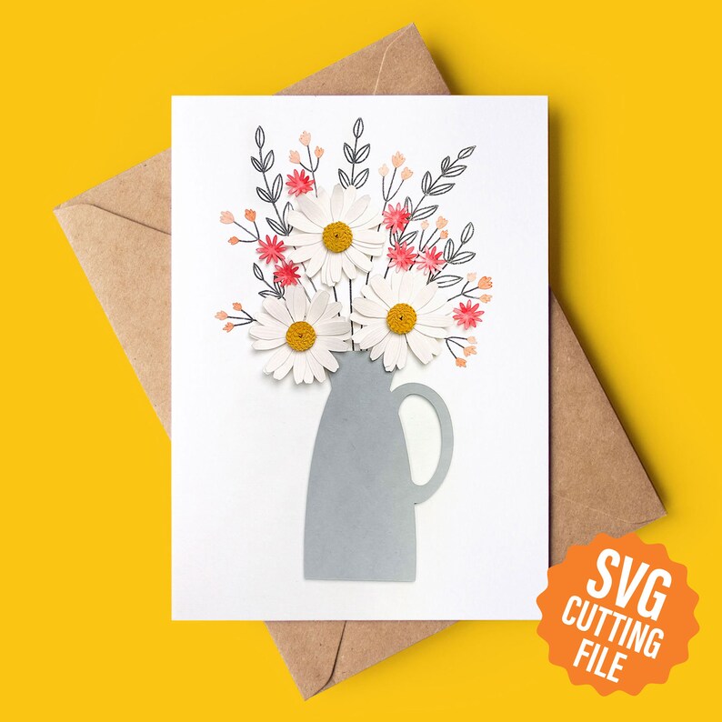 May include: A white card featuring a grey vase with a bouquet of white daisies and pink accents. The vase has a handle. The card includes the text "SVG CUTTING FILE" in a circle.