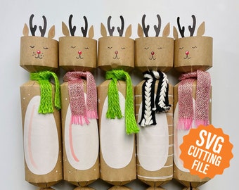 May include: A collection of five Christmas crackers, each decorated as a reindeer. The reindeer have brown paper heads with antlers, closed eyes, and red noses. The crackers have green, pink, and black and white scarves. The image includes the text "SVG CUTTING FILE".