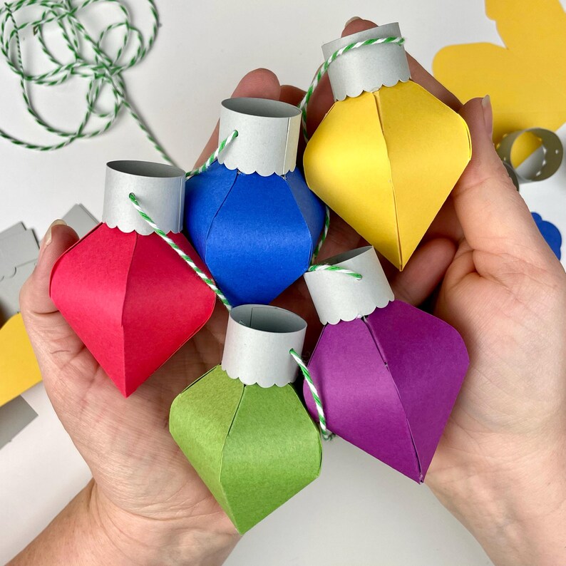 May include: Five paper Christmas ornaments in different colors, strung together with twine. The ornaments are red, blue, yellow, green, and purple.