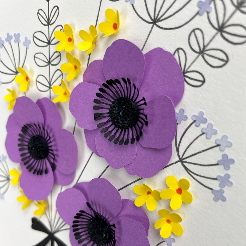 May include: Close-up of a paper craft bouquet with purple flowers and yellow flowers. The flowers are made of paper and have a 3D effect.
