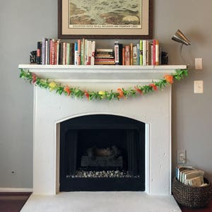 Pu&ograve; includere: Un camino in pietra bianca con un camino nero e una ghirlanda di fiori arancioni e gialli. Il camino &egrave; decorato con libri e una lampada.