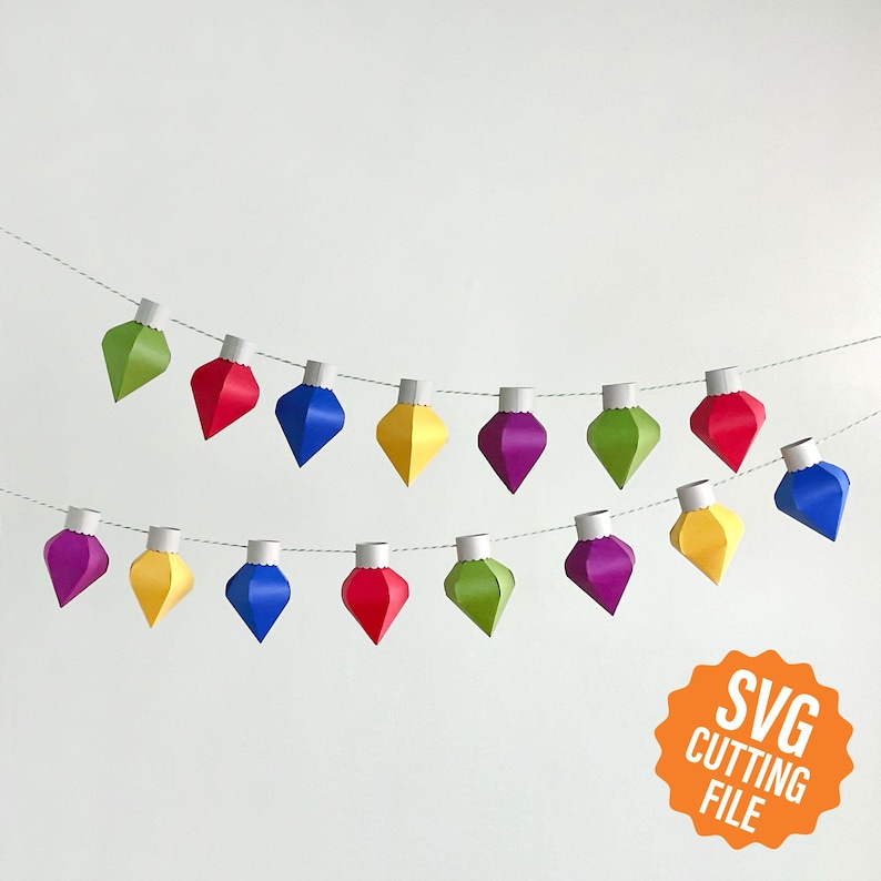 May include: A string of paper Christmas lights with red, green, blue, yellow, and purple ornaments. The lights are strung on a white string and are hanging from a white wall. The text "SVG CUTTING FILE" is in the lower right corner of the image.