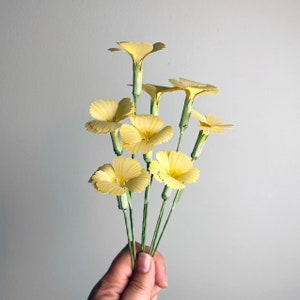 May include: A bouquet of yellow paper flowers with green stems. The flowers are arranged in a fan shape and have a delicate, ruffled appearance.