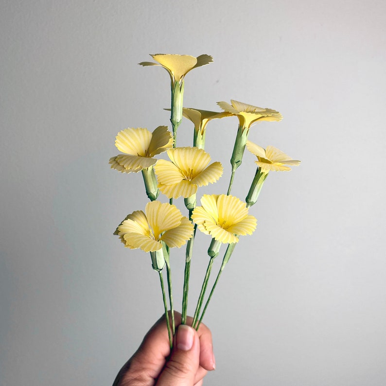 May include: A bouquet of yellow paper flowers with green stems. The flowers are arranged in a fan shape and have a delicate, ruffled appearance.