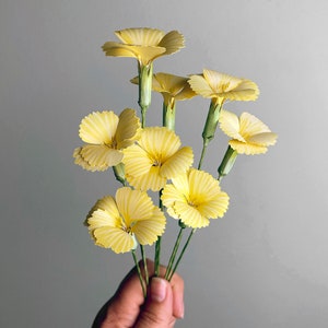 May include: A bouquet of yellow paper flowers with green stems. The flowers are arranged in a fan shape and have a delicate, layered appearance.