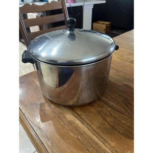 May include: A stainless steel stockpot with a polished finish, featuring two black side handles and a matching lid with a black knob. The cylindrical pot has a smooth, reflective surface and a sturdy construction, designed for cooking various food items.