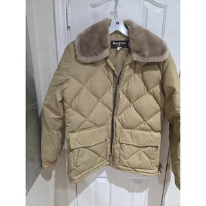 May include: A tan quilted jacket featuring a diamond-patterned stitch design, a full-length front zipper, and two front flap pockets. The jacket includes a wide, plush, light brown faux fur collar and a black interior label reading Tempco.