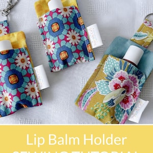 May include: Three fabric lip balm holders with metal keychains. Two holders feature a pink, blue, and white floral pattern with yellow lining. One holder features a mustard yellow, blue, and pink floral pattern with blue lining. Each has a white Sarah Cee tag.