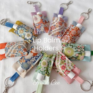 May include: Several lip balm holders with floral fabric designs in shades of orange, blue, and green. Each holder has a strap and a silver keyring. The image includes the text "Lip Balm Holders" and "Sarah Cee".